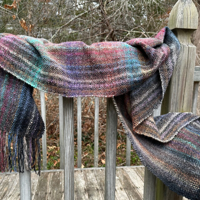 A photo of a handwoven wrap draped on a fence post.