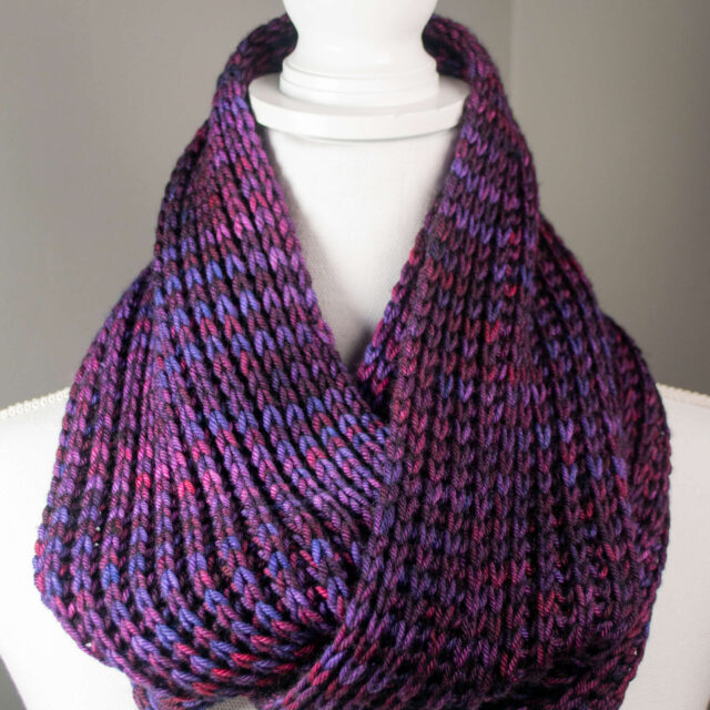 A photo of a a hand knitted brioche infinity scarf on a headless manikin.
