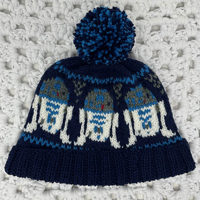 A photo of a hand knitted R2D2 colorwork hat on white crocheted background.