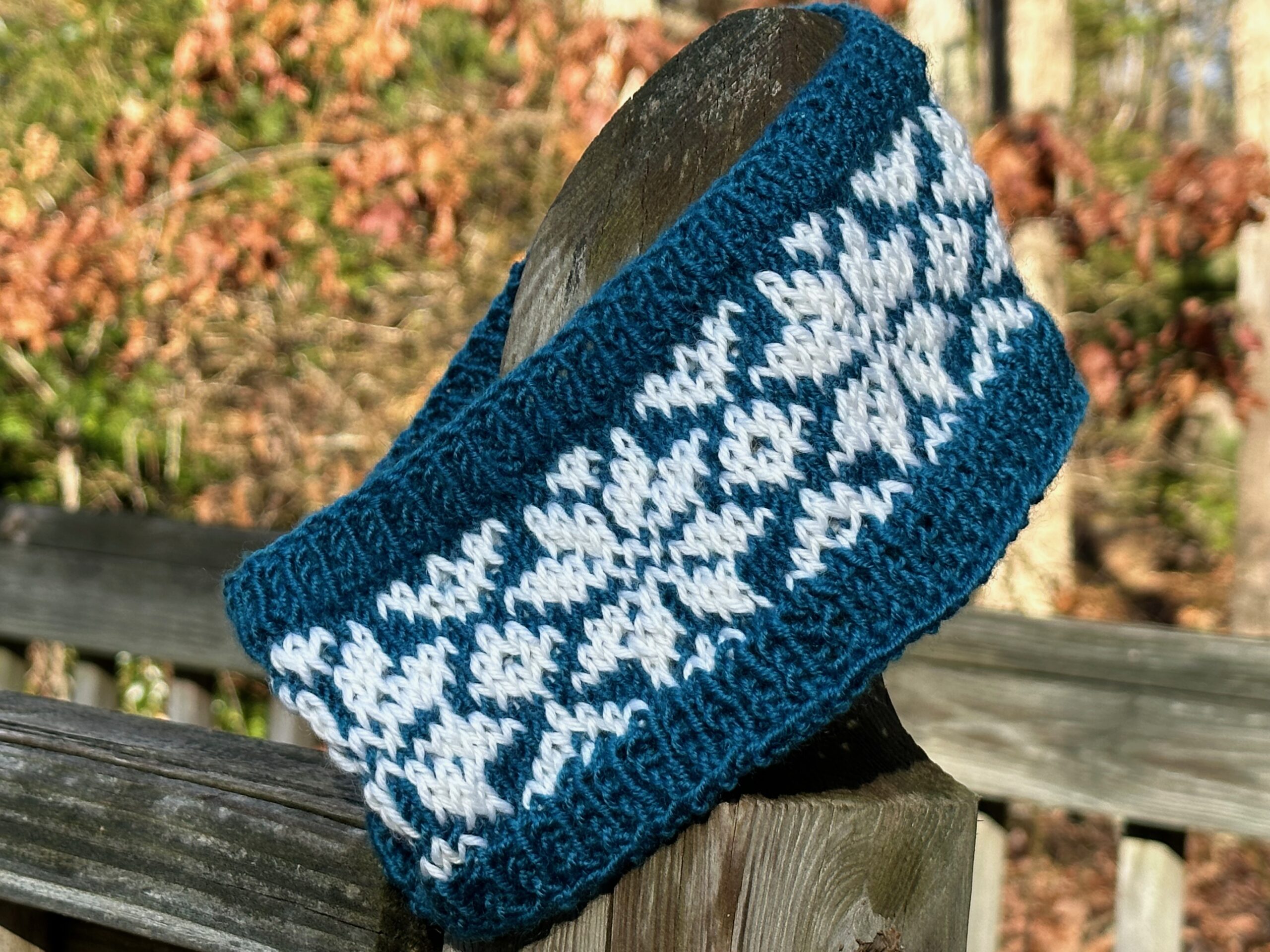 A photo of hand knitted stranded colorwork ear warmers on a fencepost.