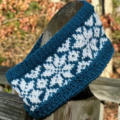 A photo of hand knitted stranded colorwork ear warmers on a fencepost.